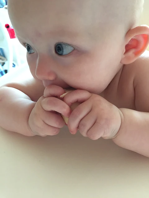 A baby clutching a bit of banana and eating it