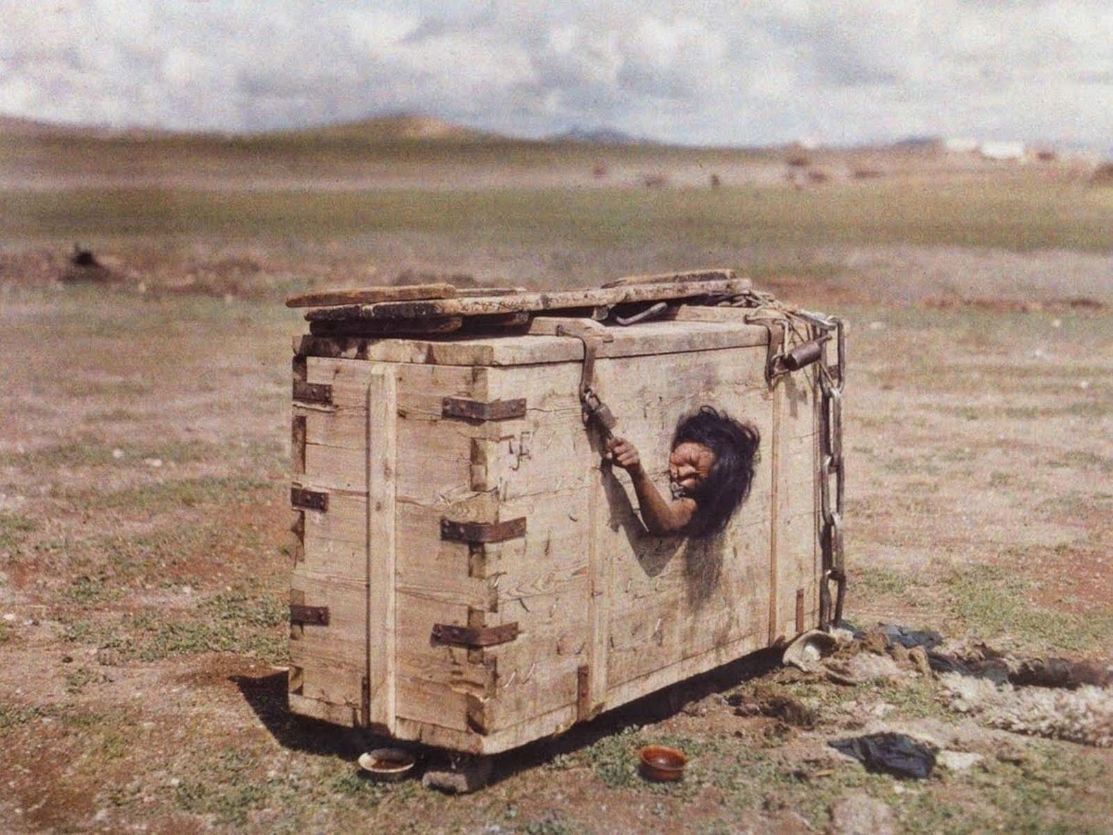 A Mongolian woman reaches out from the porthole of a crate in which she is imprisoned, c. July 1913. Note the swastika on the corner next to the lock.