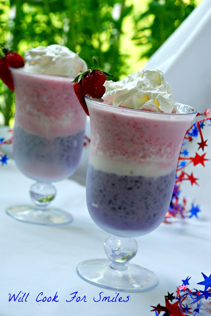 two red white and blue milkshake with whipped cream and a strawberry on top as garnish 