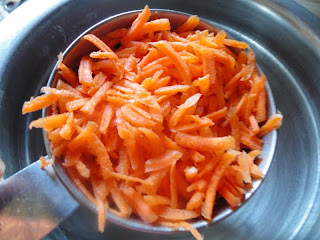 A measuring cup filled with carrots held over a stainless steel mixing bowl.