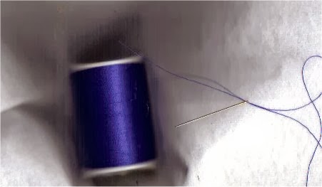 Blue thread on spool with needle threaded ready to cut
