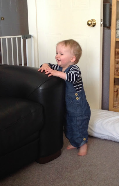 baby stood by sofa laughing