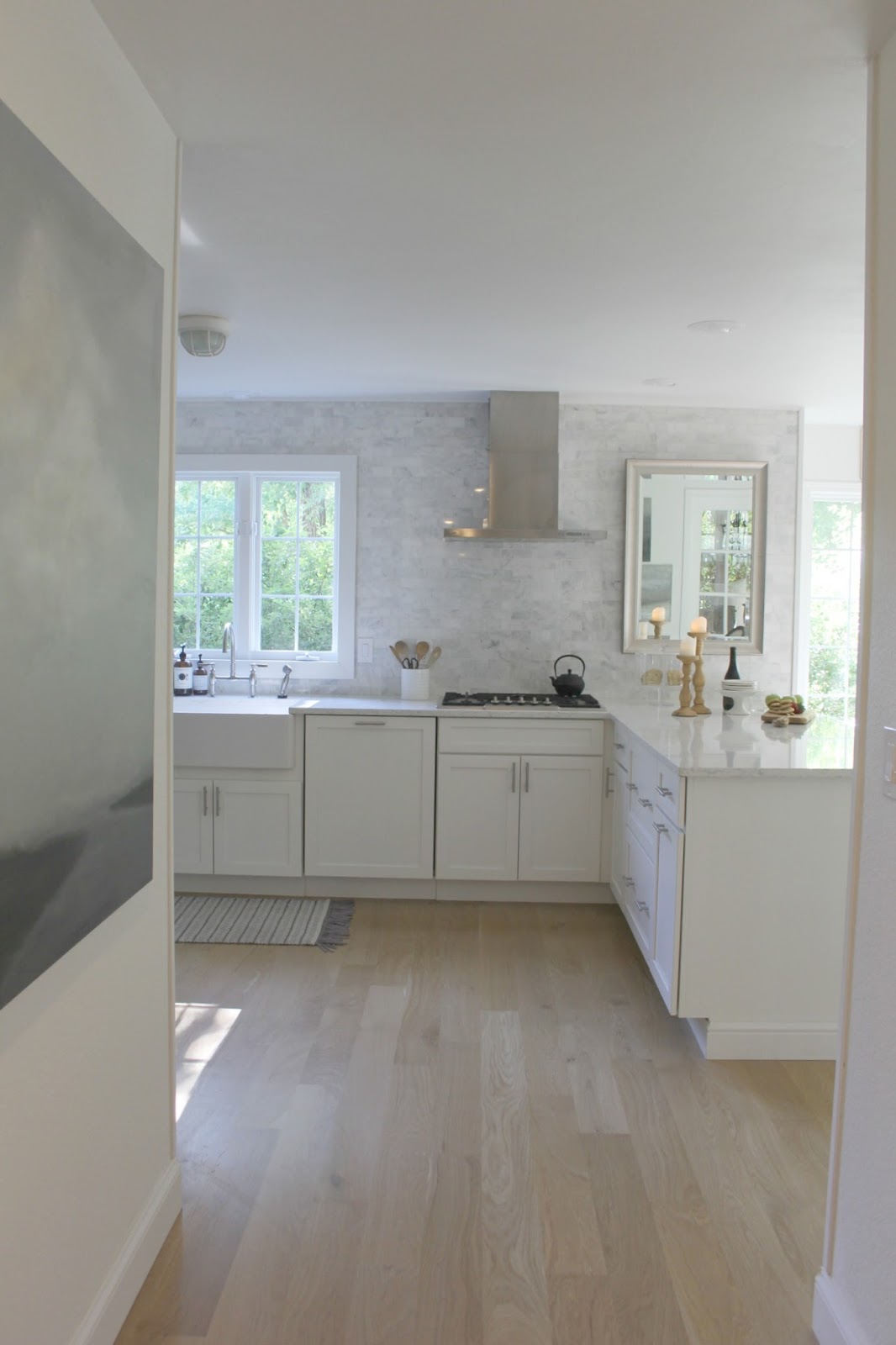 Serene white kitchen with white oak hardwood flooring. Shaker kitchen cabinets, Viatera quartz countertop (Minuet). Carrara subway tile taken to the ceiling. Come tour my home and consider low cost timeless decorating approaches to simple decor.