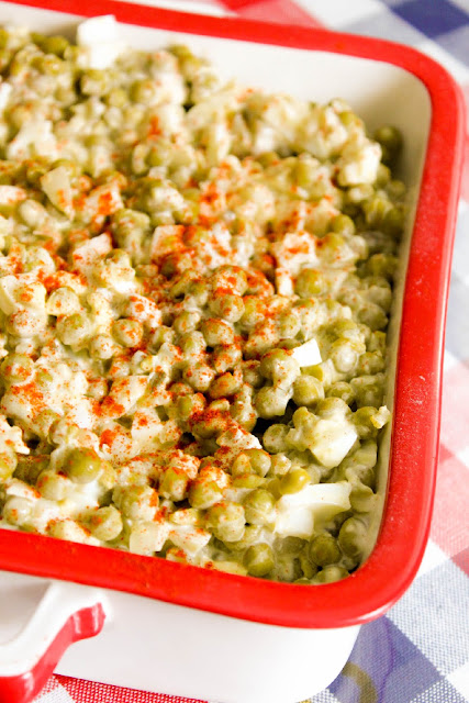 This photo shows pea salad in a square red and white serving pan. 