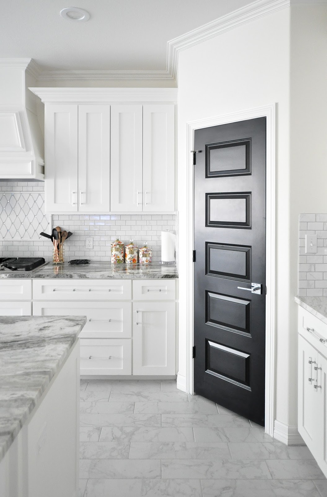 White shaker cabinet kitchen with lucite acrylic handles and a black pantry door.
