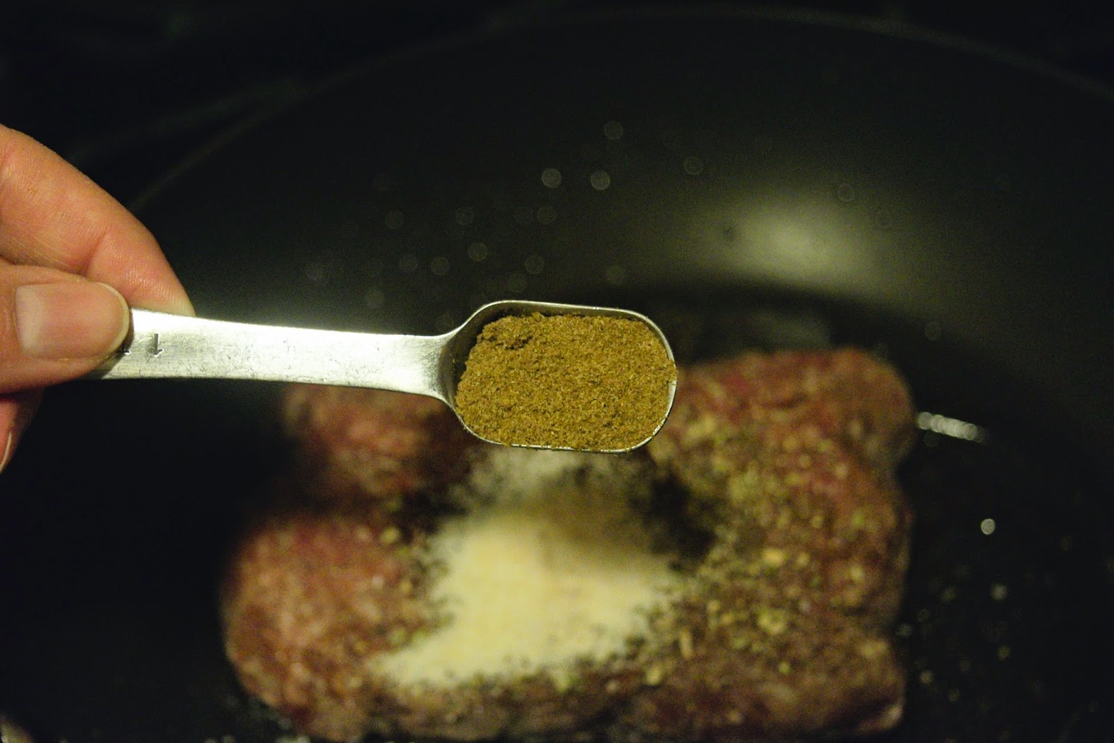 Cumin being added to the ground beef in the pan. 