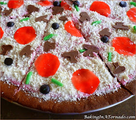April Fools Peanut Butter and Jelly Pizza Cookie, a fun trick to play on the family. Peanut Butter Cookie, jelly in the frosting and lots of fun sweet toppings. | Recipe developed by www.BakingInATornado.com | #AprilFoolsDay #recipe #cookie