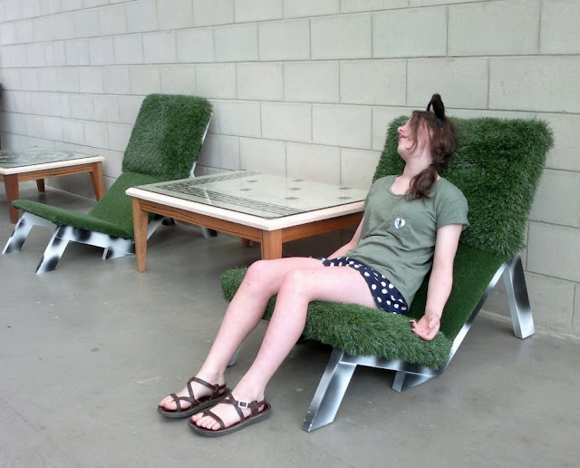 Two outdoor chairs with lawn covered cushions. The legs are painted white with black spots like cowhide.