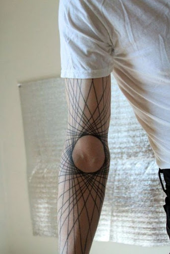 Essa tatuagem, que lembra um spirograph criação, ou raios em uma roda de bicicleta, retrata uma série de linhas em torno de um núcleo central, a tatuagem é composto de tinta preta e a peça é apresentada no utente do antebraço.