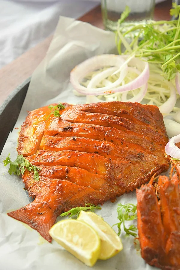 Black plate with white paper and served Masala Fried Fish (Grilled Pomfret)
