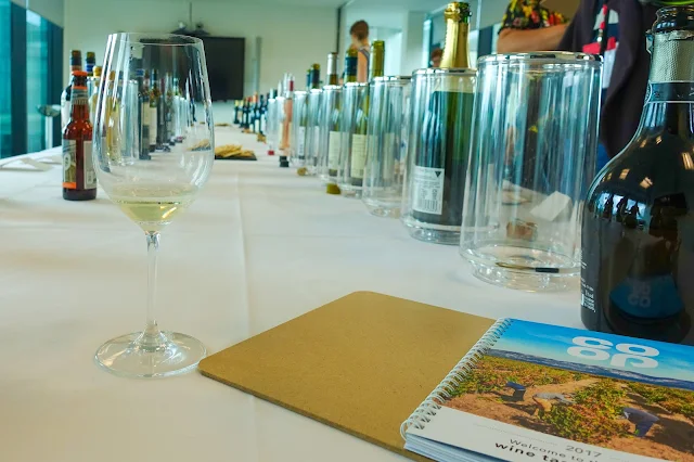 A co-op tasting guide and wine glass in the foreground and 2 lines of wine bottles in the background