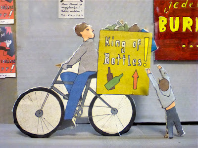 Aus Pappe ausgeschnitten und bemalt: Mann auf dem Rad, das viele Flaschen transportiert, darauf ein Schild: "King of the bottles"