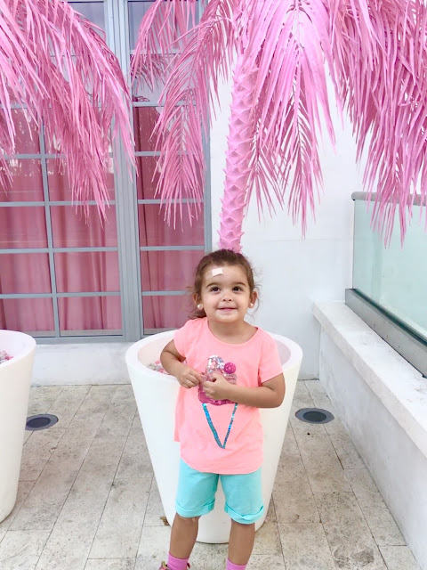 Little girl standing in front of a potted pink palm tree