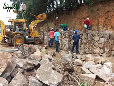 Execução do muro de pedra rústica sendo o tipo de pedra moledo na face do muro e no enchimento a pedra rachão. Muro de pedra com junta seca sem cimento nas juntas.