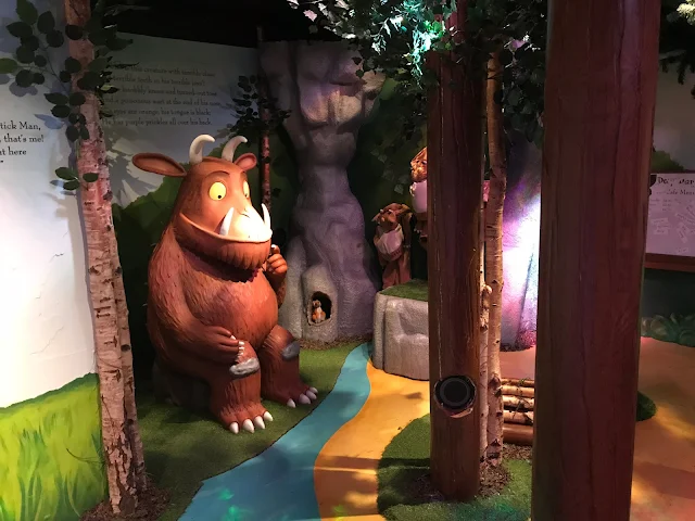 A model of the Gruffalo surrounded by trees and a painted stream and grass