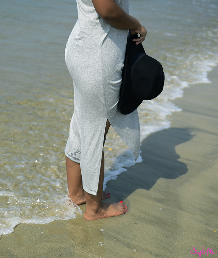 An image of a woman standing by the sea on the shore of a beach wearing a maxi dress and holding a hat on a summer holiday break in Goa, India