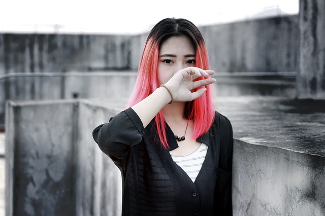 Young woman with black and pink hair, looking lost, back of hand covering her mouth