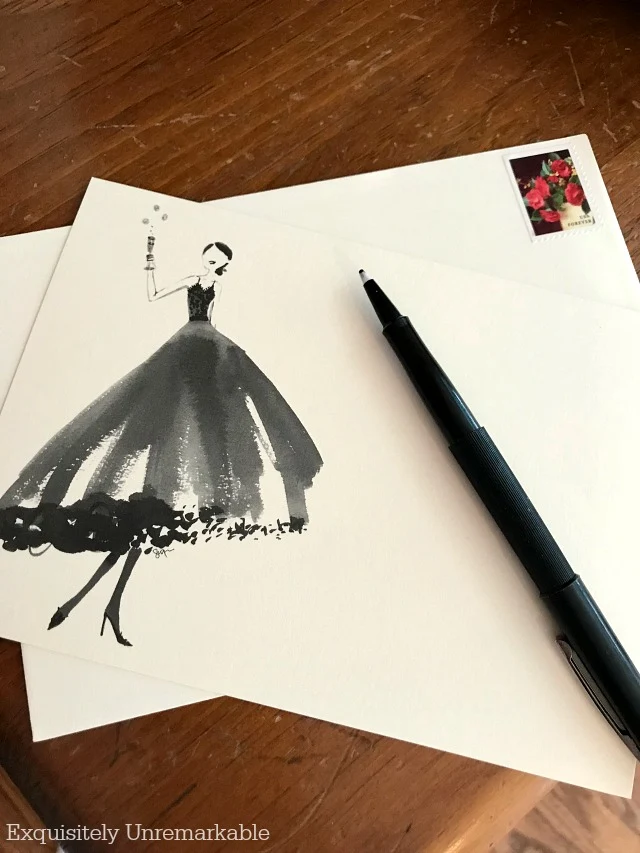 Stationary with a drawing of woman in a dress, toasting, next to a pen and envelope
