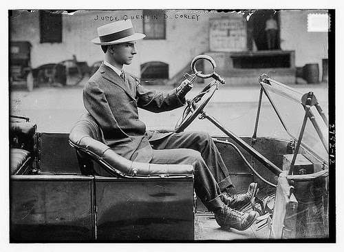 1920s black and white photo of a man driving a car with prosthetic arms.