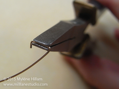 Bending the wire in flat nose pliers to form the first side of a triangle jump ring.