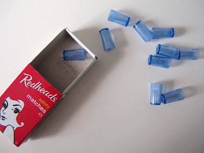 Matchbox with nine miniature blue glasses or vases spilling out of it.
