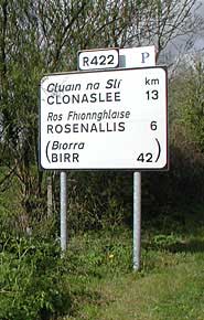 Picture 1: A bilingual road sign showing both English and Irish place names in black text on a white sign.