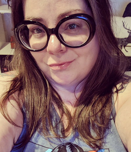 image of me from mid-cheest up, with my hair down around my shoulders, wearing a grey-blue tanktop and large, black-framed glasses