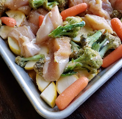 corner of sheet pan with raw chicken and veggies ready to cook