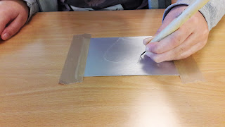 A mão de uma aluna a desenhar com a ponta seca o seu desenho na chapa de metal