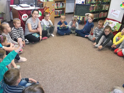 Dzieci siedzą w kole i rozmawiają z bibliotekarką
