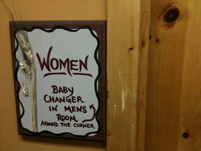 Handlettered sign for a women's room saying the baby changing table is around the corner in the men's room