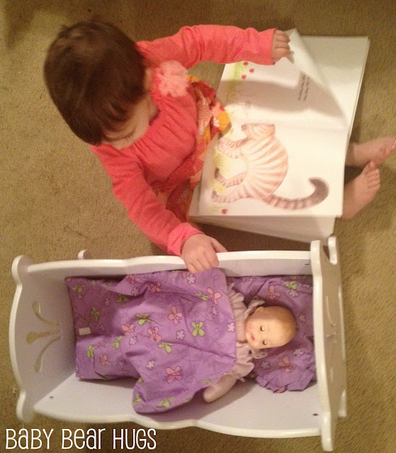 toddler with Kidkraft Lil' doll cradle and madame alexander doll reading a book