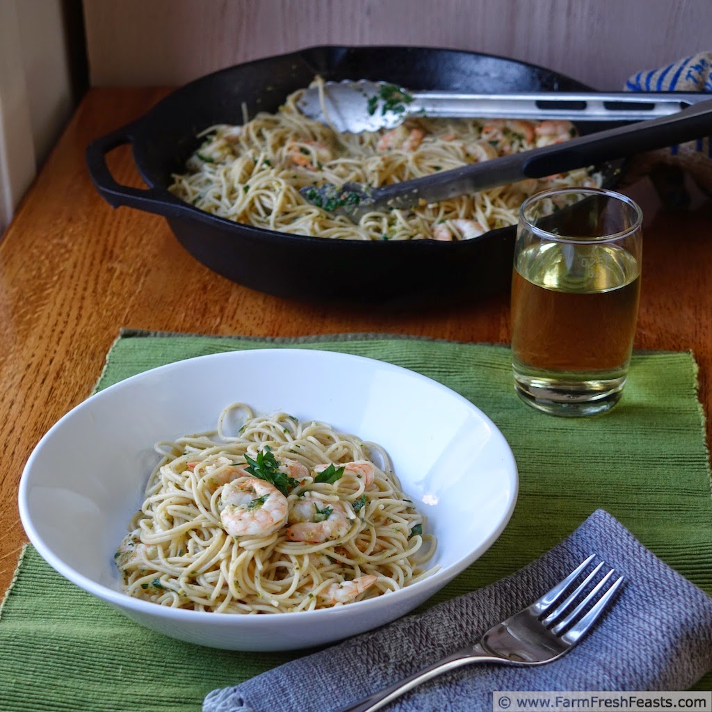 Image of a cast iron skillet with shrimp, garlic scape pesto, and parsley in a wine/butter/lemon sauce over pasta. 