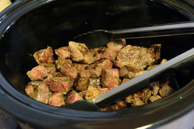 The browned beef being added to the slow cooker.