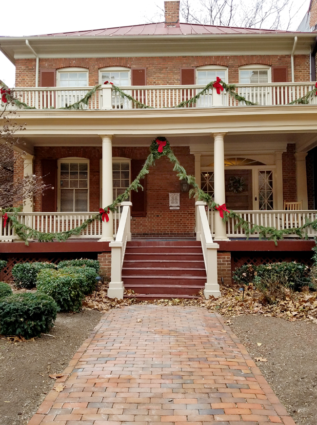 brick house with front porch decorated for Christmas - off center main door.
