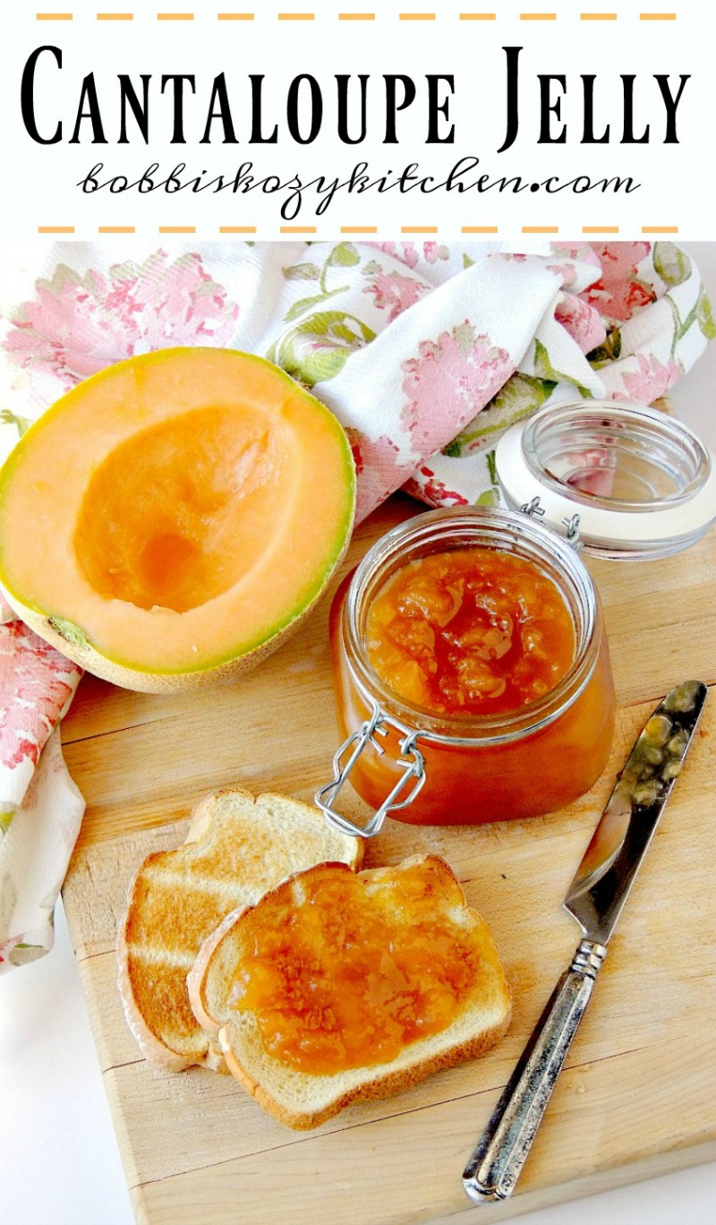Cantaloupe Jelly in a glass jar with a fresh cantaloupe half and toast beside it on a wooden cutting board with a floral towel.