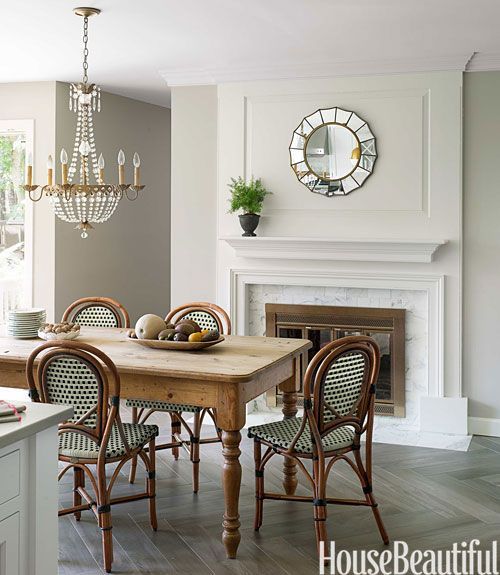 Beautiful green bistro style chairs surround a rustic knotty pine farm table in an elegant dining room with marble surround fireplace and crystal chandelier. The herringbone flooring adds another layer of French elegance. #frenchcountry #Parisian #herringbone