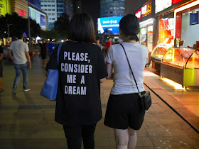 two young women walking together; one is wearing a "Please, consider me a dream" shirt