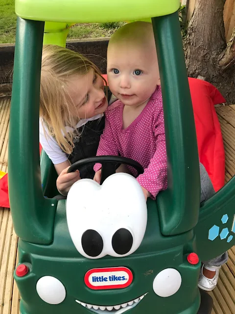 Little trying to climb into the dino Little Tikes car while her big sister is sitting in it it.
