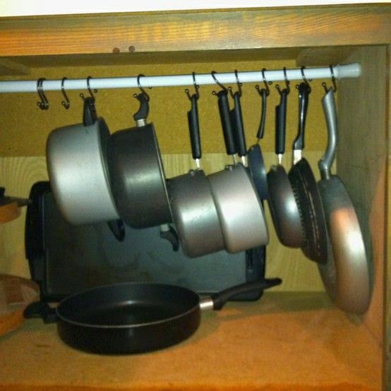 Pots and pans hanging by curtain rod inside cupboard