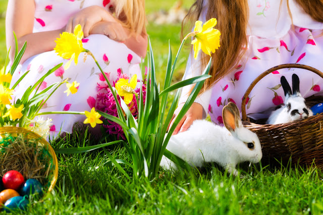 Two children with two pet rabbits and a basket of easter eggs on the grass