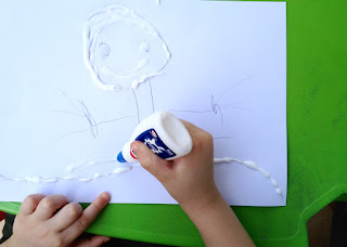 Criança desenhando com cola, antes de jogar a areia