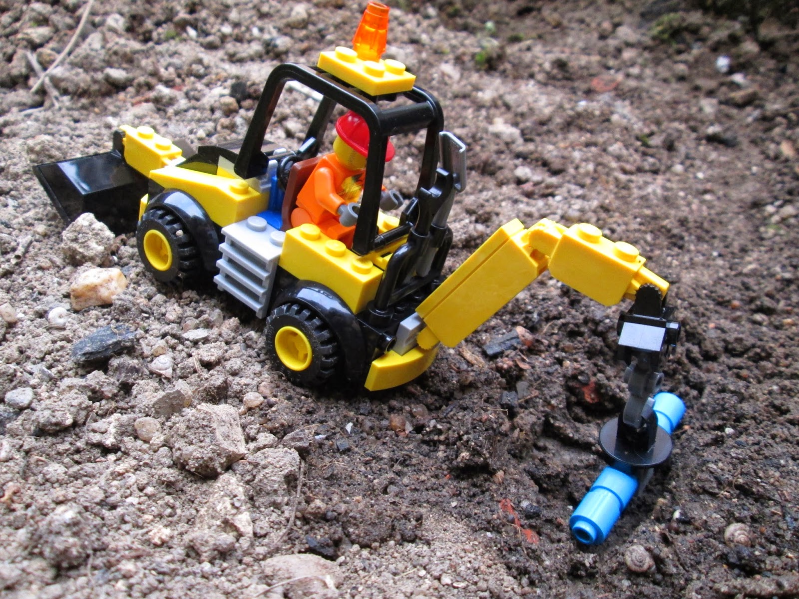 Diorama LEGO em cenário real, representando trabalhos de remoção de terras com máquina para substituição de rutura em conduta de água.