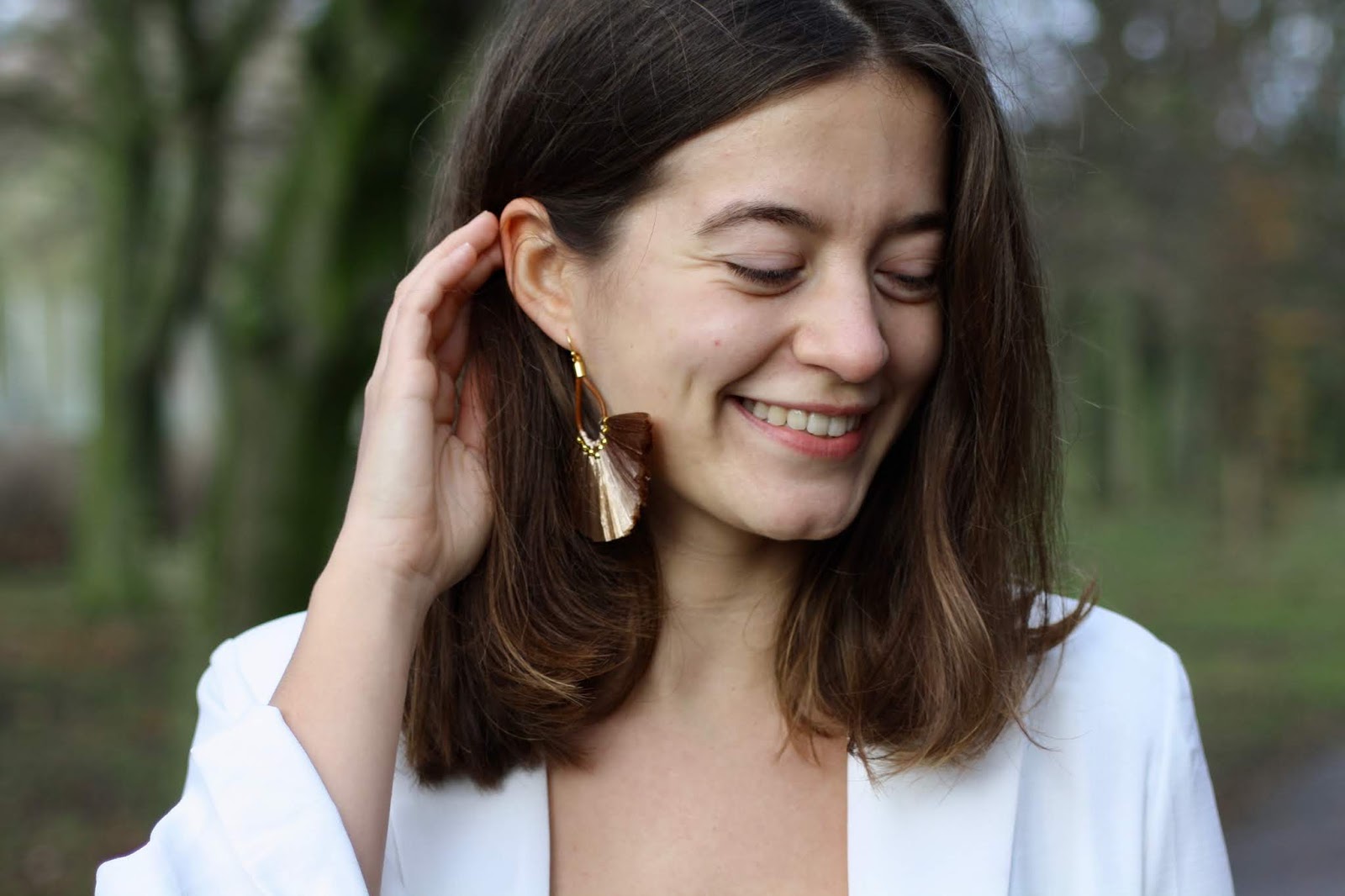 abbey, smiling, brushes her hair behind her ear, showing off taupe tassel earrings