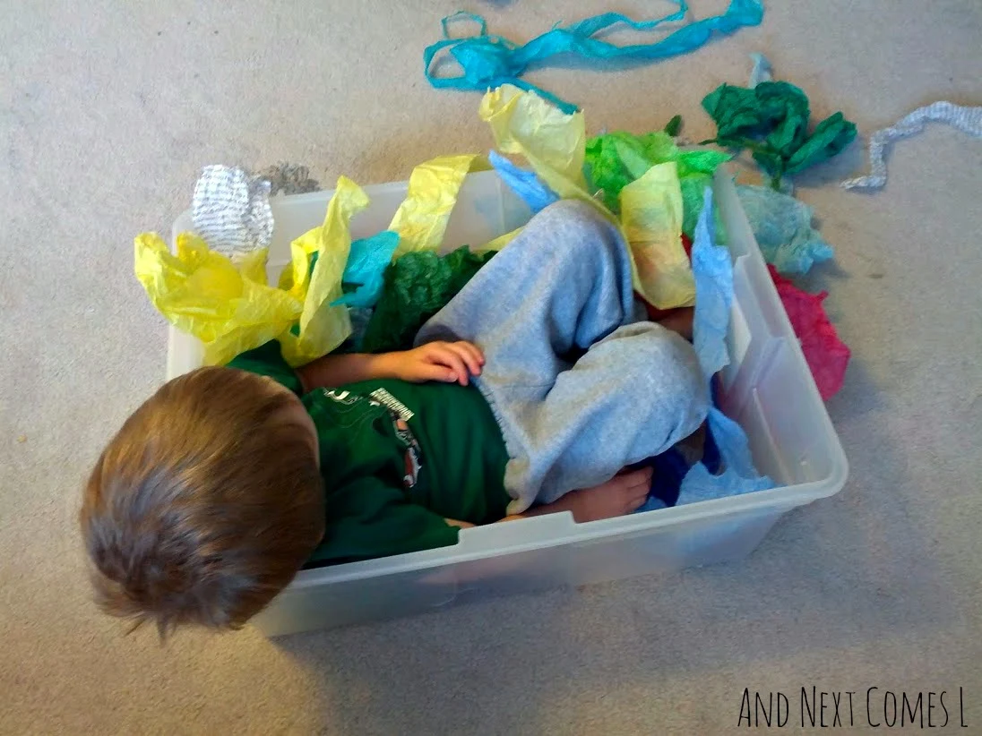 J sitting in tissue paper sensory bin from And Next Comes L