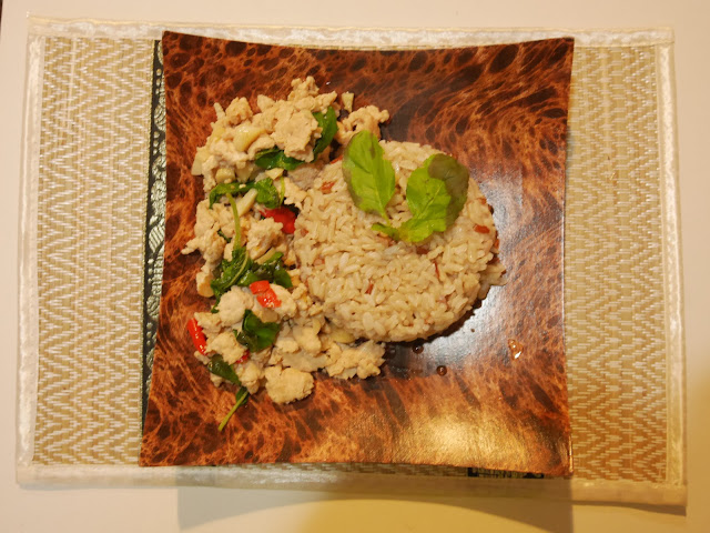 Thai stir fried chicken with red chillies and holy basil served with rice on a wooden plate