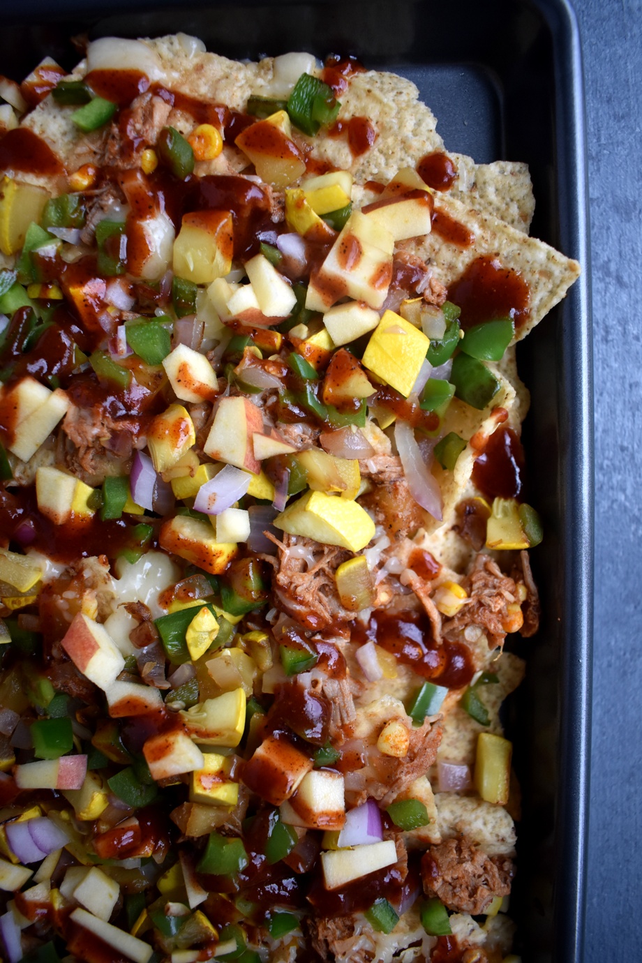 Loaded BBQ Pulled Pork Nachos are loaded with shredded pork, melted cheese, sauteed corn, bell peppers and onions and crunchy apples with a homemade drizzled smoky barbecue sauce! www.nutritionistreviews.com