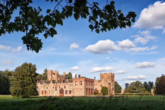 Oxburgh Hall captured from under the boughs of a tree Oxburgh Hall stately home in the Norfolk countryside under a blue sky