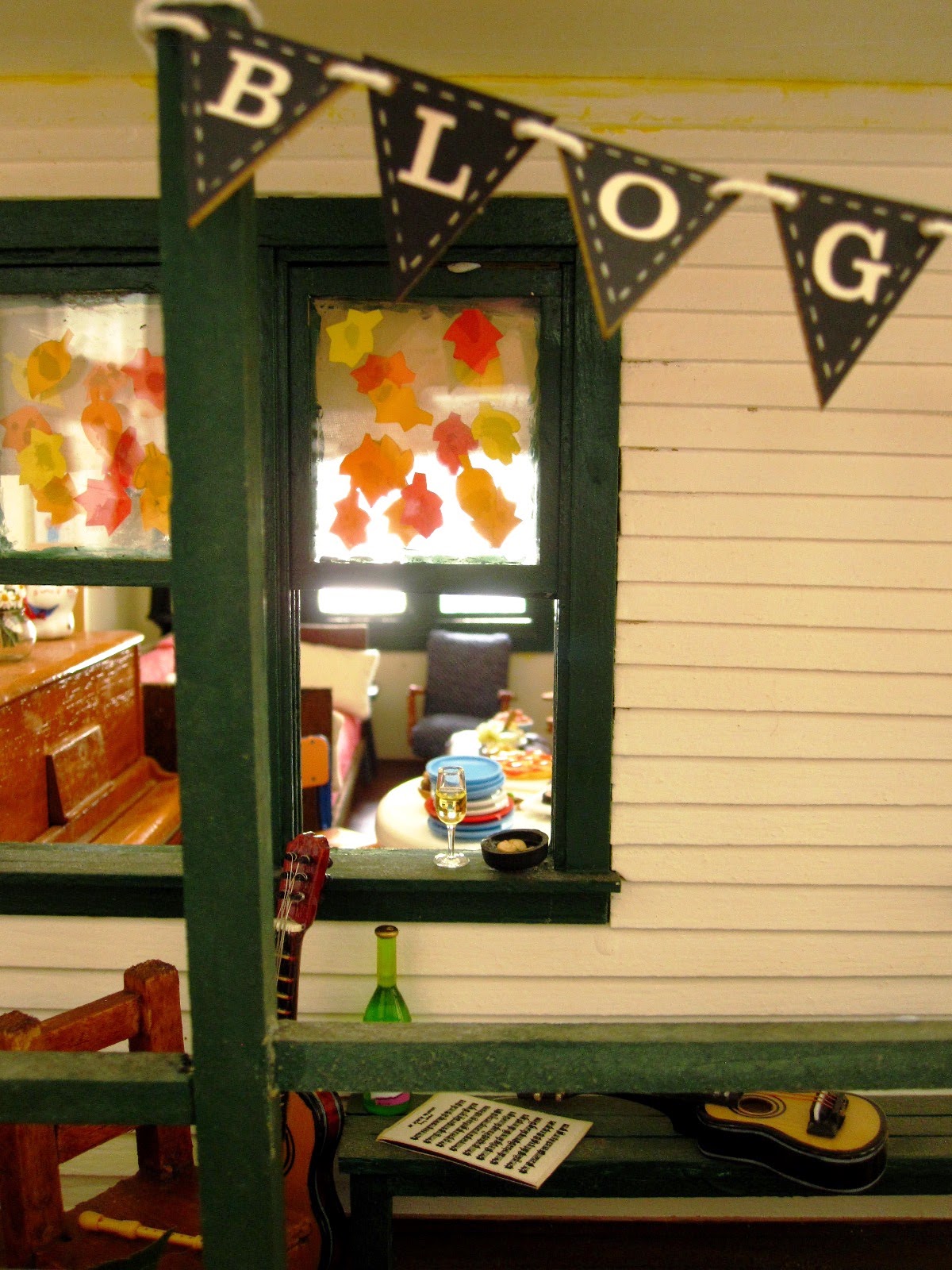 View of a miniature dolls' house veranda with a selection of musical instruments arranged on it. In front, tied to a paost, is bunting reading 'blog'.