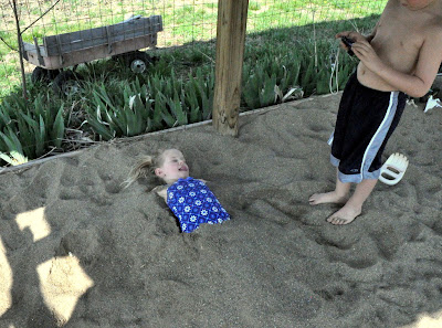 girl buried up to her waste in sand.